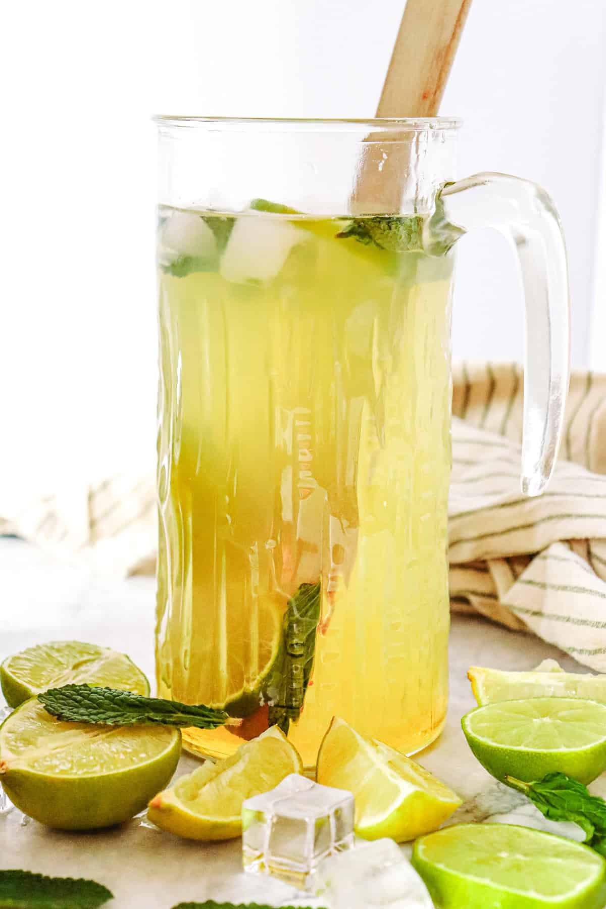 A glass pitcher of Virgin Mojito iced tea with lime, mint leaves, and ice cubes, surrounded by sliced limes and fresh mint&mdash;refreshing mocktail recipe inspiration.