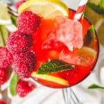 A glass of red drink with raspberries and lemons, perfect for trying a refreshing raspberry mojito mocktail recipe.