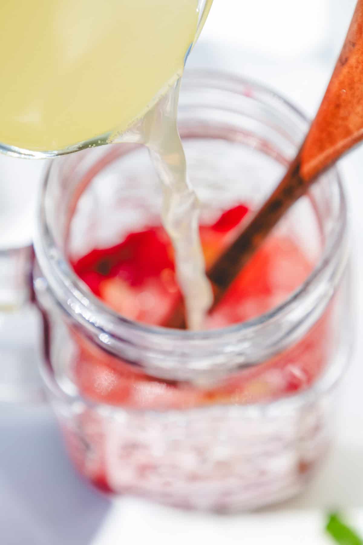 Lemonade being poured into a mason jar filled with strawberries, with a wooden spoon inside&mdash;perfect inspiration for your next raspberry mojito mocktail recipe.