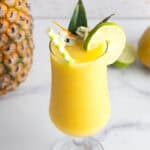 A yellow Mango Mocktail smoothie in a glass, garnished with a lime slice, flowers, and striped straws.