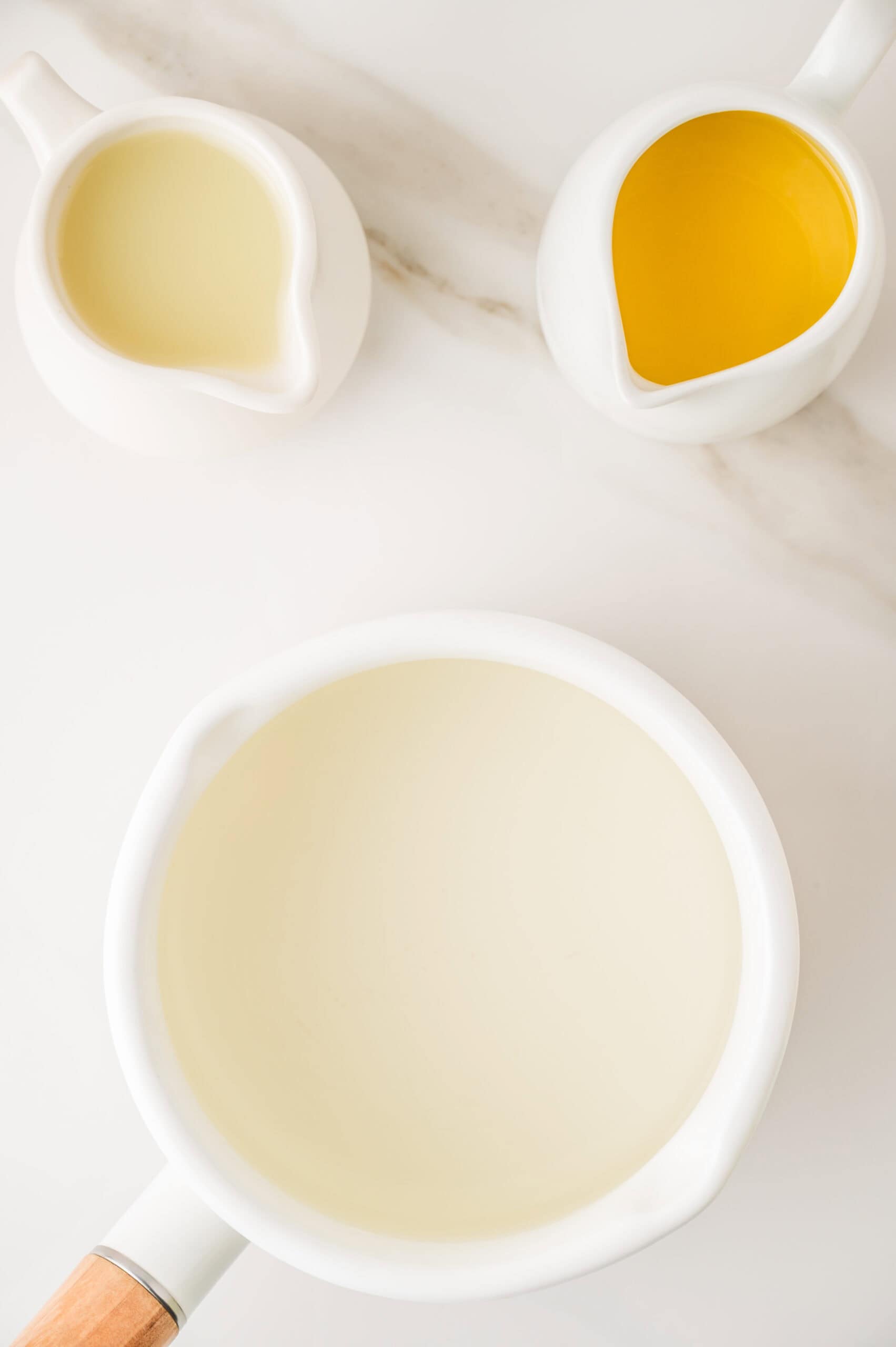 Three white containers filled with liquid, viewed from above; one with yellow liquid&mdash;perfect for a homemade orangeade recipe&mdash;and two with white liquid.