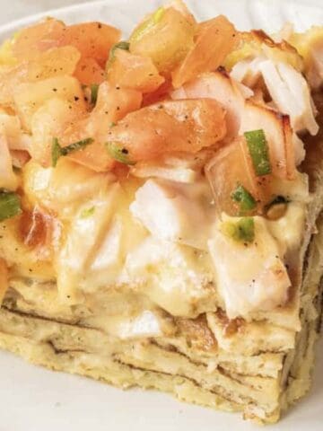 A slice of layered egg casserole topped with diced tomatoes and herbs on a white plate.