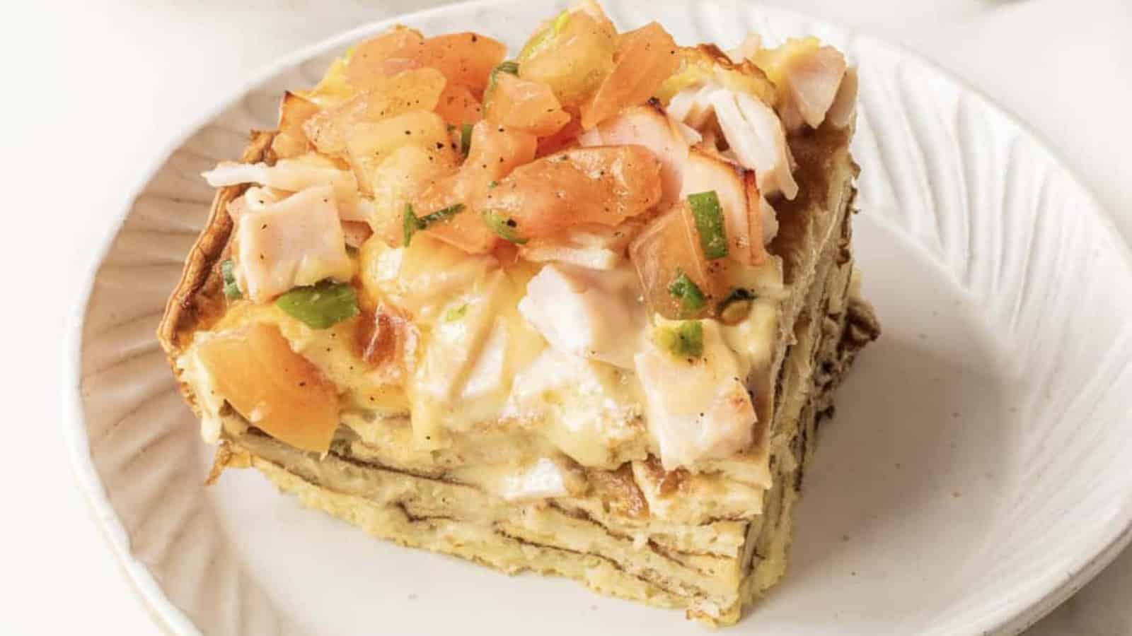 A slice of layered egg casserole topped with diced tomatoes and herbs on a white plate.
