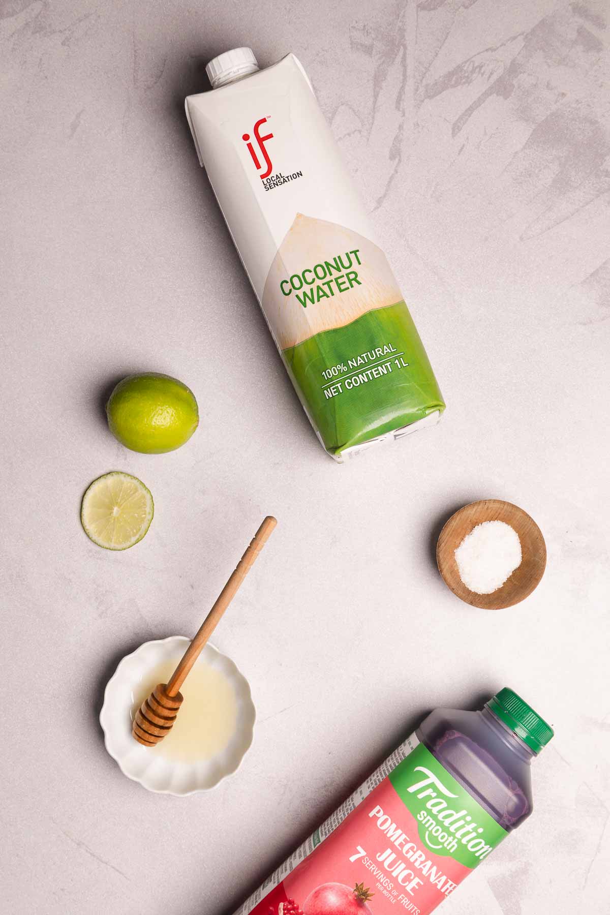 Coconut water, pomegranate juice, lime, salt, and honey on a light surface&mdash;an inviting mocktail recipe packed with natural electrolytes, viewed from above.