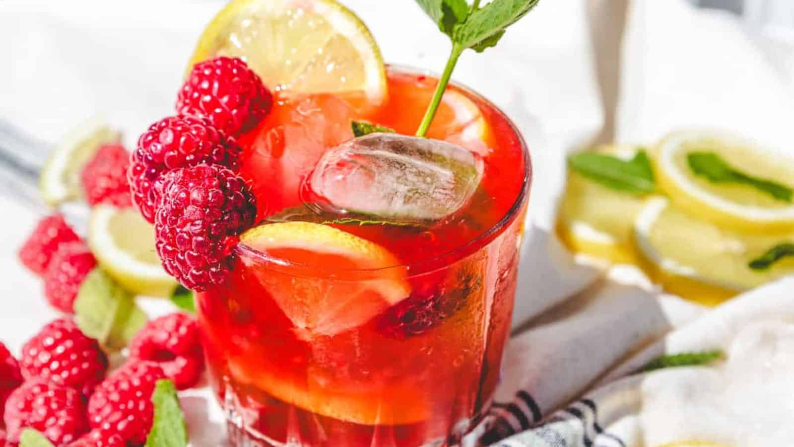 A close-up of a red drink with ice, raspberries, lemon slices, and a sprig of mint.