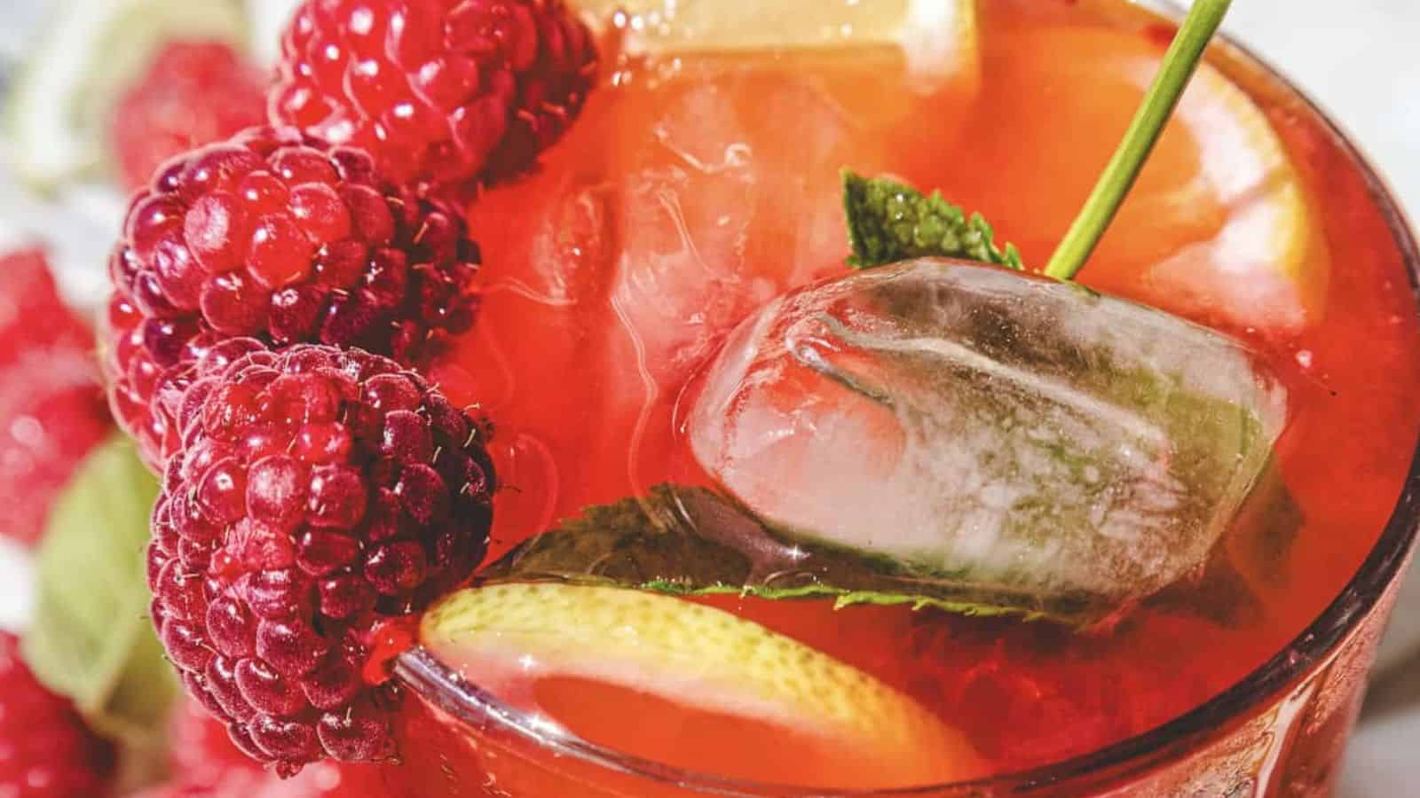 A glass of lemonade with ice, mint leaves, lemon slices, and fresh mint on a marble surface.