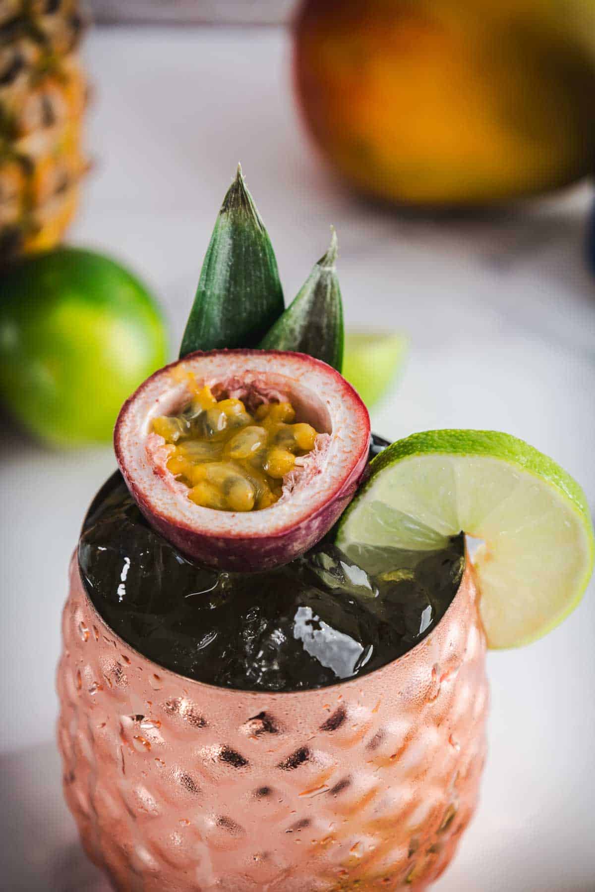 A tropical mocktail in a copper cup, garnished with a lime slice, passionfruit, and pineapple leaves&mdash;a refreshing tropical drink perfect for any occasion.