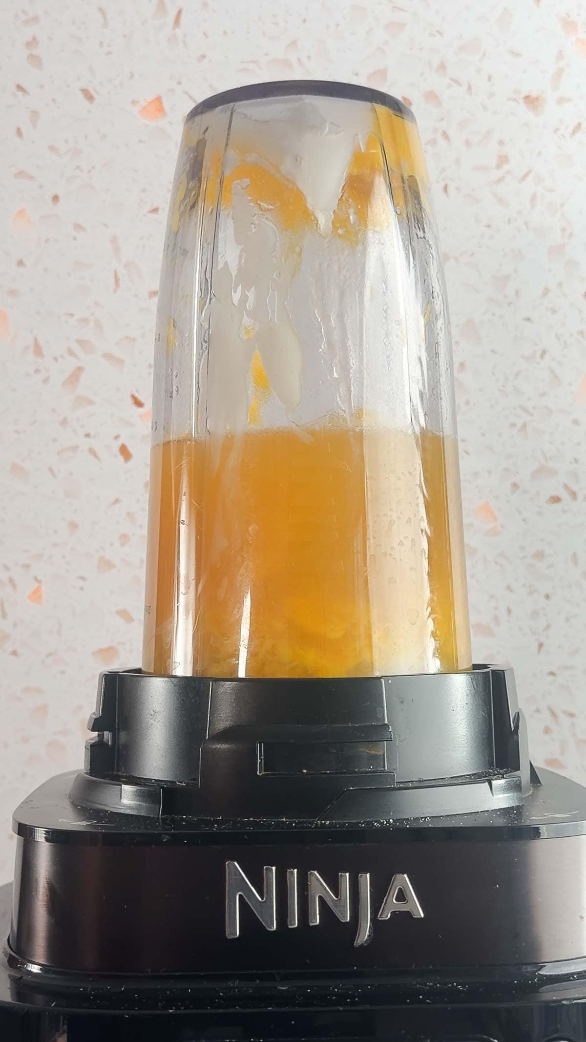A Ninja blender whirls a vibrant Mango Mocktail against a light, speckled background.