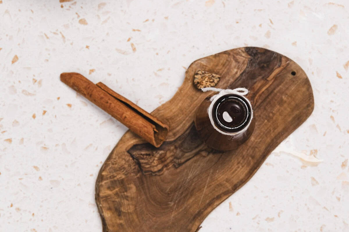 A cinnamon stick and a small brown jar of Brown Sugar Apple Crisp Syrup rest on a wooden board, placed on a light-colored surface&mdash;perfect for your next Starbucks Copycat syrup recipe.