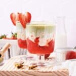 Layered strawberry and matcha drinks in glass cups, garnished with strawberry slices on a wooden board&mdash;an inviting Strawberry Matcha Recipe perfect for refreshing any occasion.