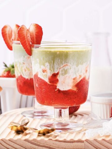 Layered strawberry and matcha drinks in glass cups, garnished with strawberry slices on a wooden board&mdash;an inviting Strawberry Matcha Recipe perfect for refreshing any occasion.