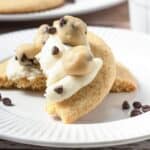 A cookie dough cookie topped with frosting, cookie dough balls, and chocolate chips on a white plate&mdash;just like your favorite Crumbl copycat treat.