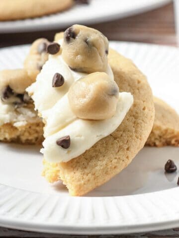 A cookie dough cookie topped with frosting, cookie dough balls, and chocolate chips on a white plate—just like your favorite Crumbl copycat treat.
