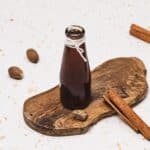 A glass bottle of Brown Sugar Apple Crisp Syrup sits on a wooden board, surrounded by nutmeg and cinnamon sticks&mdash;a perfect Starbucks copycat for your favorite fall drinks.