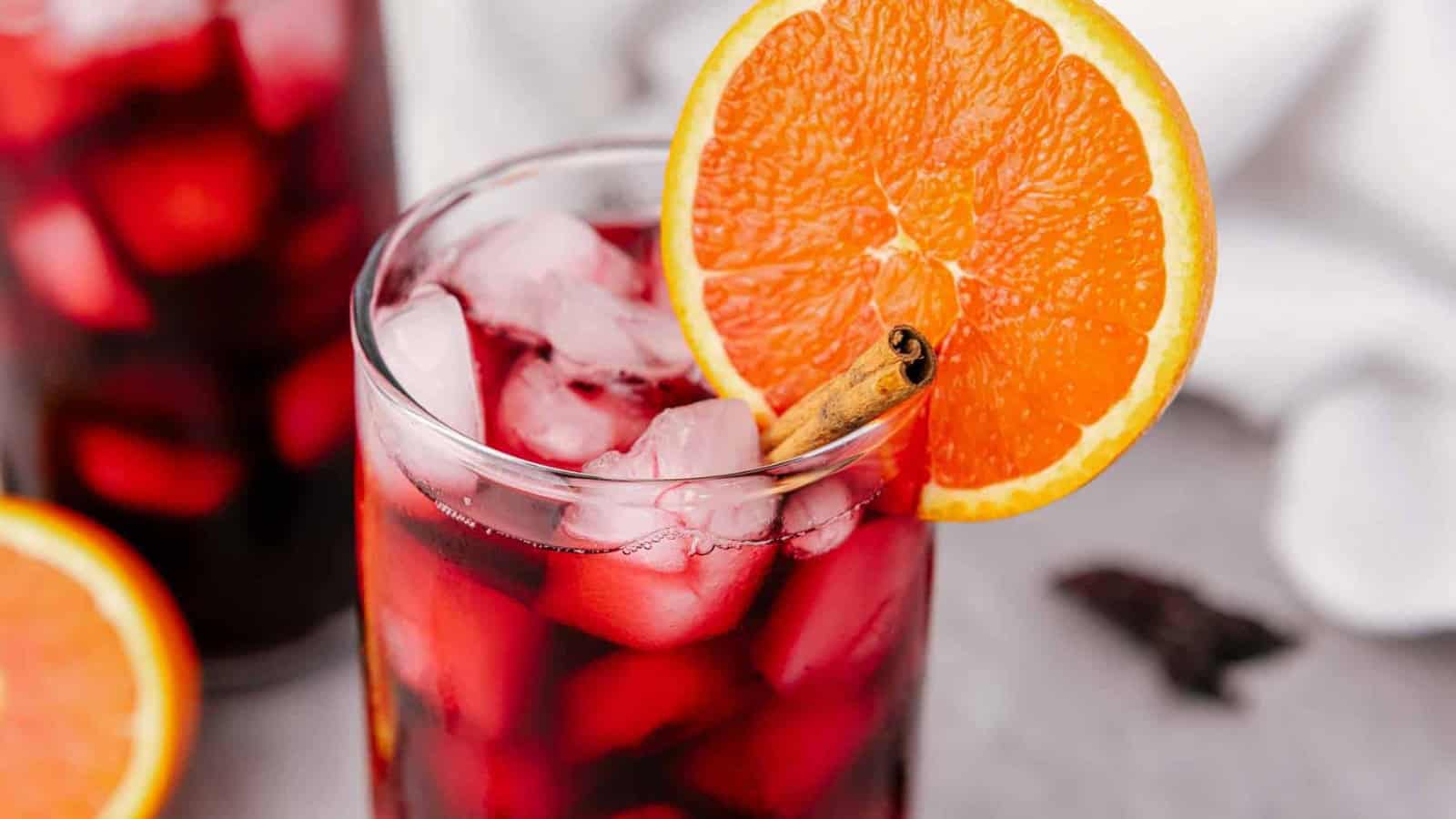 A glass of red liquid with ice and an orange slice.