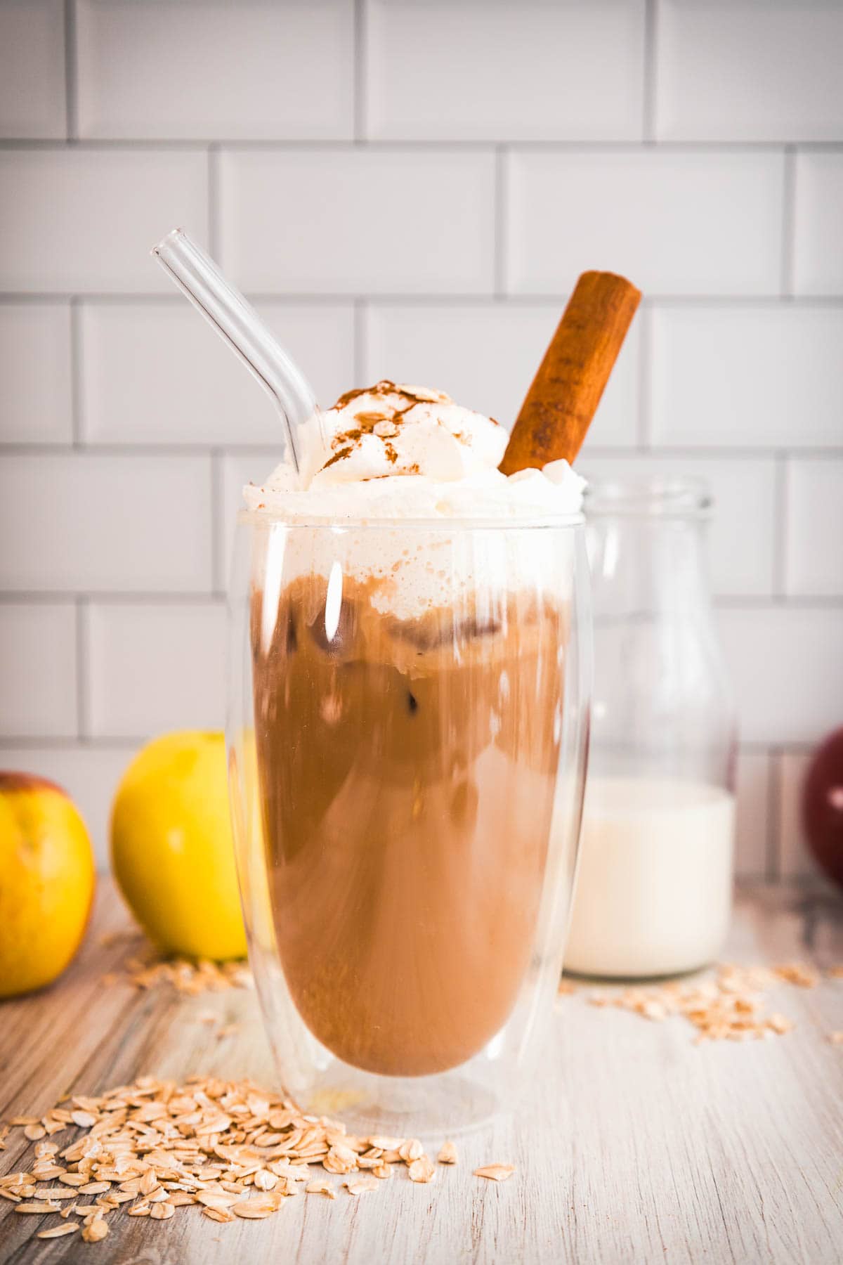 Iced coffee topped with whipped cream, cinnamon stick, oats, and apples&mdash;just like an Apple Crisp Latte. Enjoy this Starbucks Copycat with a glass of milk in the background.
