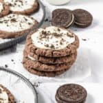 A stack of frosted Oreo cookies with white frosting and crumbs, next to classic chocolate sandwich cookies&mdash;perfect for a Crumbl Copycat treat.