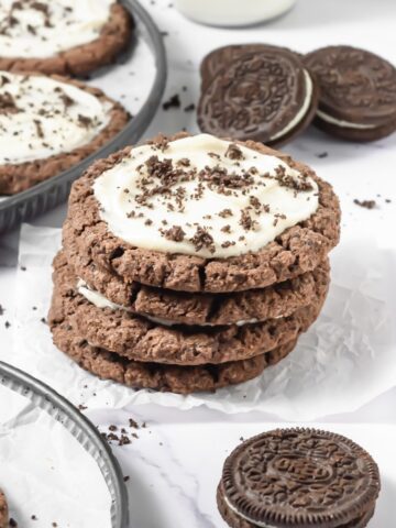 A stack of frosted Oreo cookies with white frosting and crumbs, next to classic chocolate sandwich cookies—perfect for a Crumbl Copycat treat.