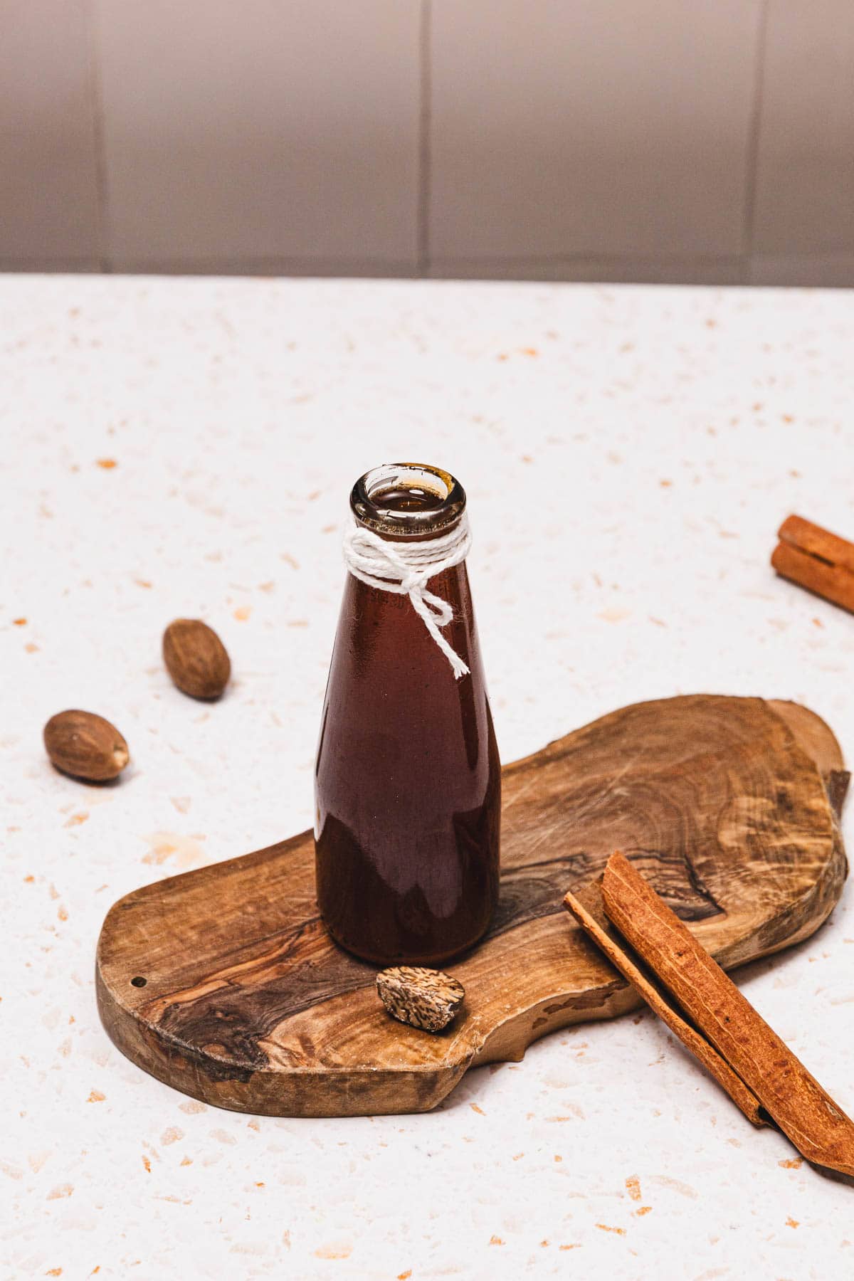 A glass bottle of Brown Sugar Apple Crisp Syrup sits on a wooden board, surrounded by whole nutmegs and cinnamon sticks&mdash;a perfect Starbucks Copycat syrup recipe for your homemade drinks.