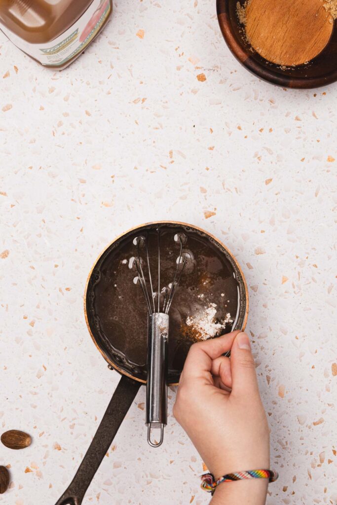 A hand holding a whisk over a bowl of chocolate, ready to craft a decadent syrup recipe inspired by Starbucks copycat creations.