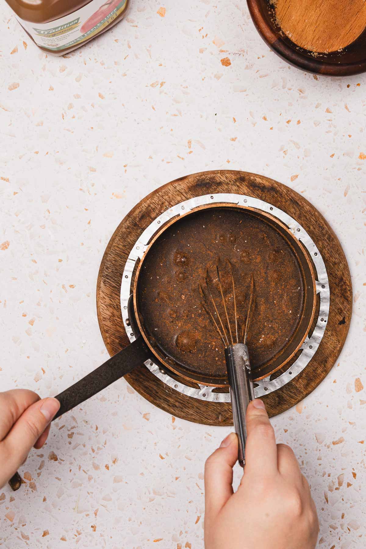 Hands whisking chocolate batter in a round pan on a wooden board, viewed from above&mdash;perfect for recreating a Starbucks Copycat treat or pairing with your favorite Brown Sugar Apple Crisp Syrup.