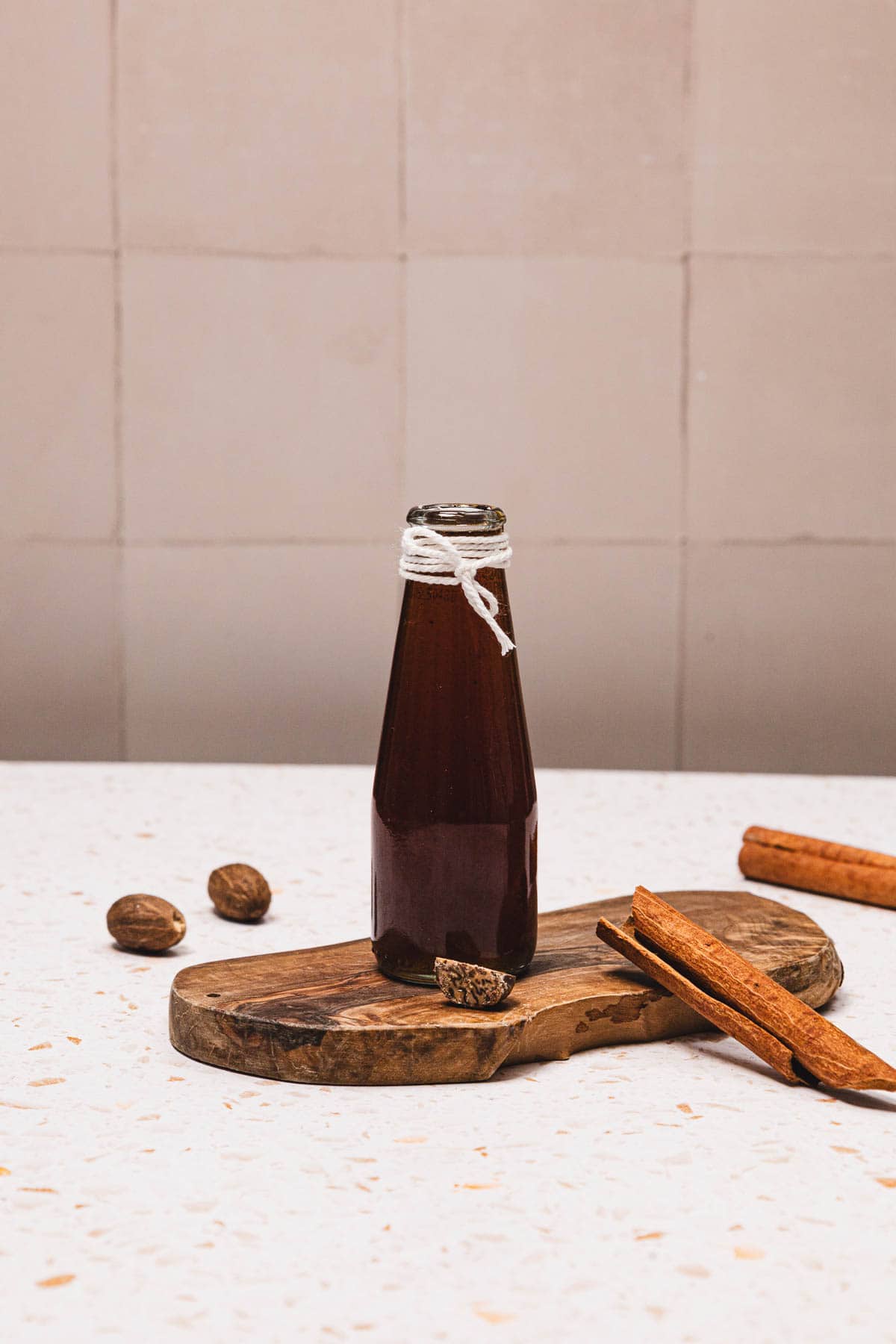 A glass bottle of dark liquid on a wooden board with cinnamon sticks and nutmeg hints at a delicious Brown Sugar Apple Crisp Syrup, perfect for recreating your favorite Starbucks Copycat syrup recipe at home.