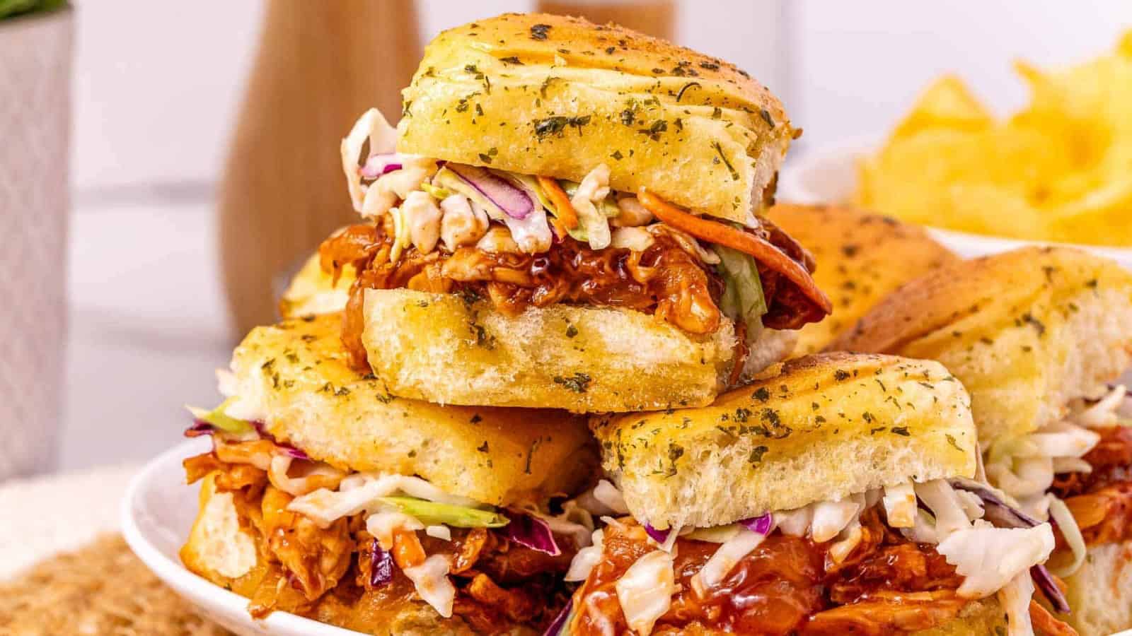 Several barbecue chicken sliders with coleslaw on golden buns are arranged on a wooden surface.
