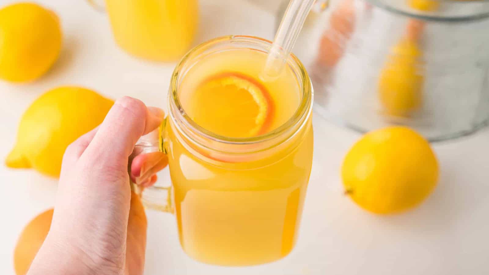 A glass jar of orange juice with a straw and slice of orange, surrounded by fresh citrus fruits.