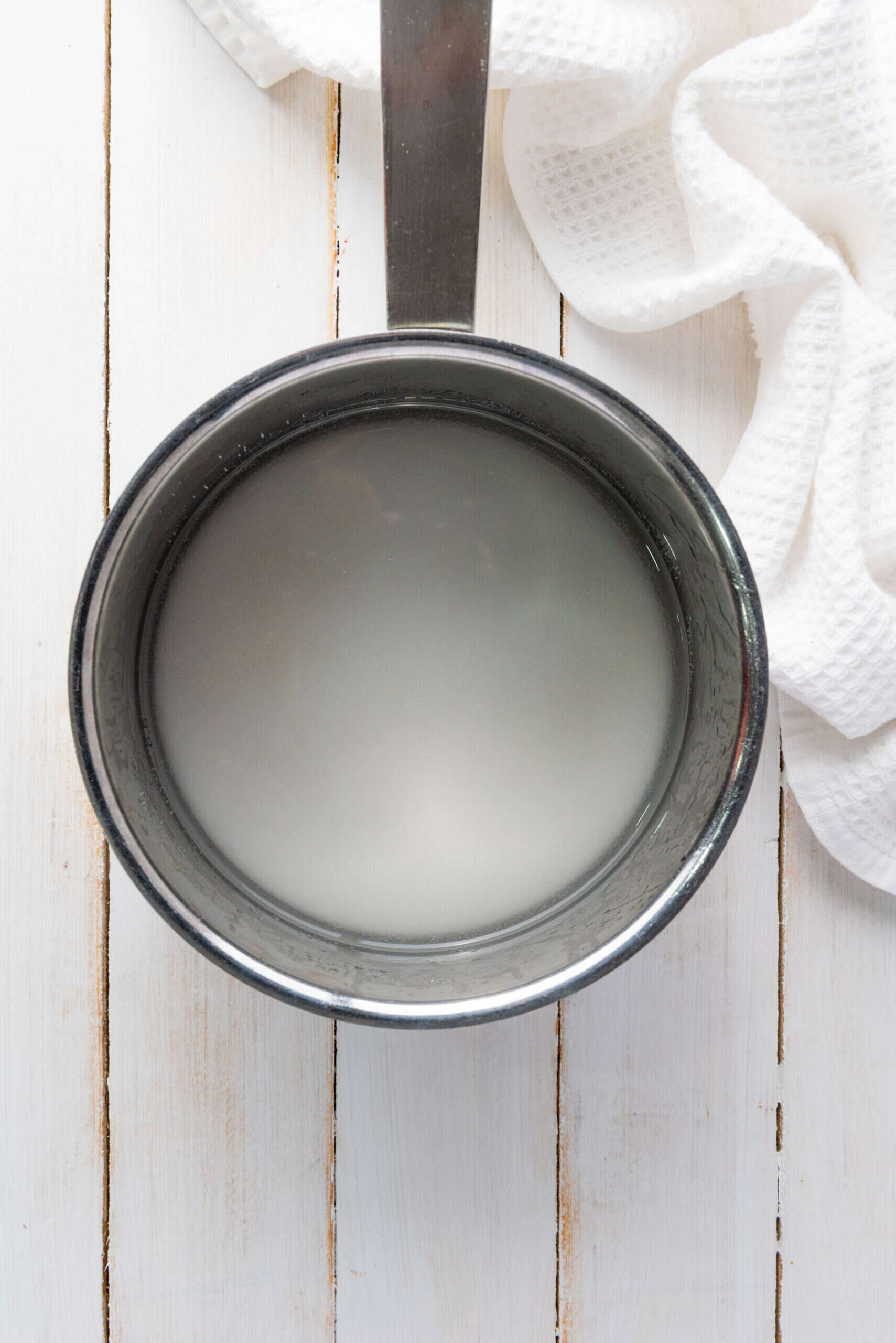 A pot of cloudy water, perfect for crafting a fresh homemade lemonade, sits on a white wooden surface next to a textured white cloth.
