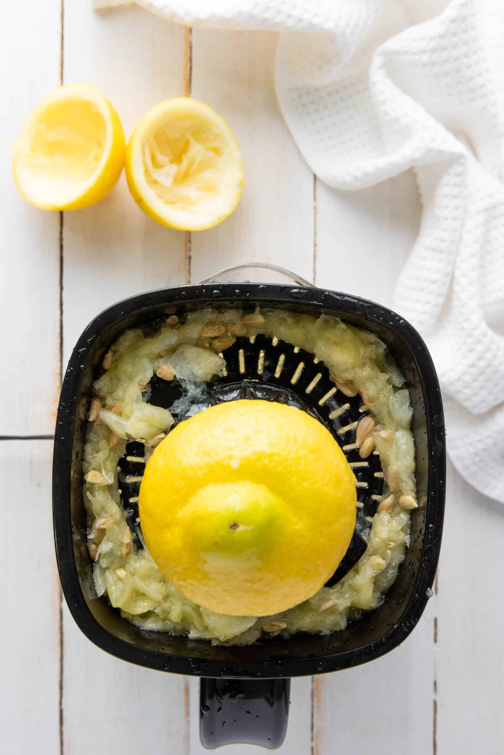 Overhead view of a lemon being juiced in a black juicer, with squeezed lemon halves and a white towel nearby&mdash;perfect prep for your favorite Homemade Lemonade Recipe.