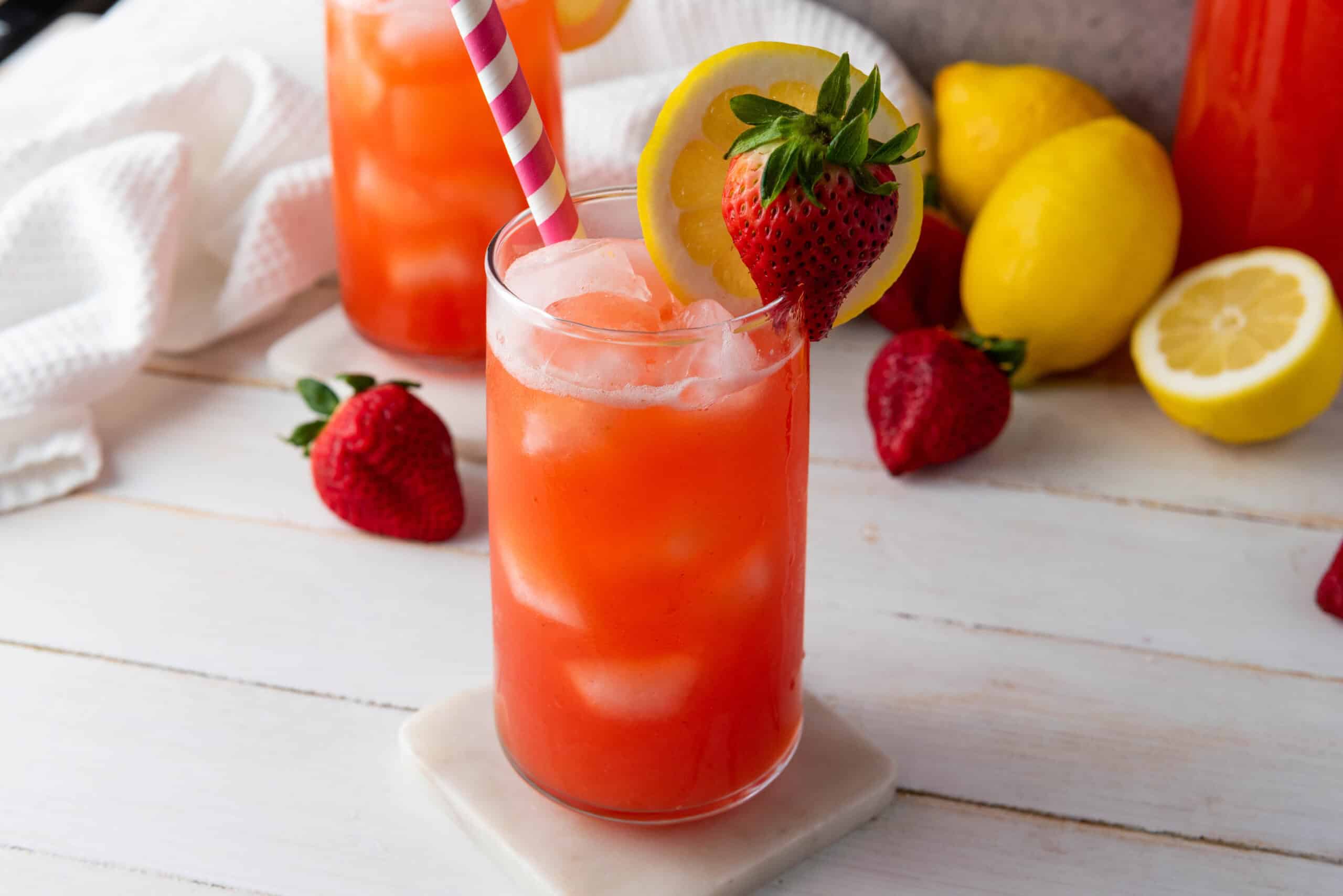A glass of homemade strawberry lemonade with a striped straw, garnished with a lemon slice and strawberry.