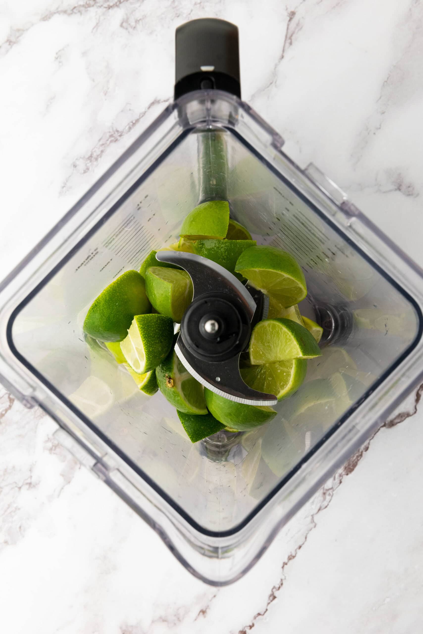 Top view of cut limes inside a blender on a white marble surface, ready to be blended into a refreshing Brazilian Limeade.