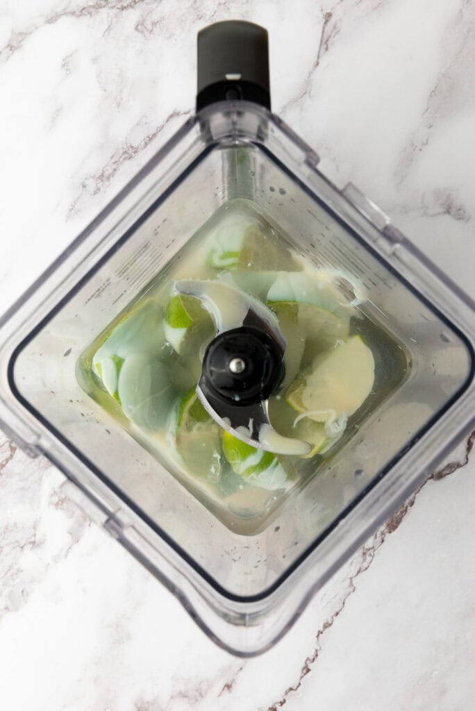 Overhead view of eggshells and water inside a blender on a marble countertop, similar to the first steps in making Brazilian limeade, a refreshing Brazilian lemonade made with fresh limes.
