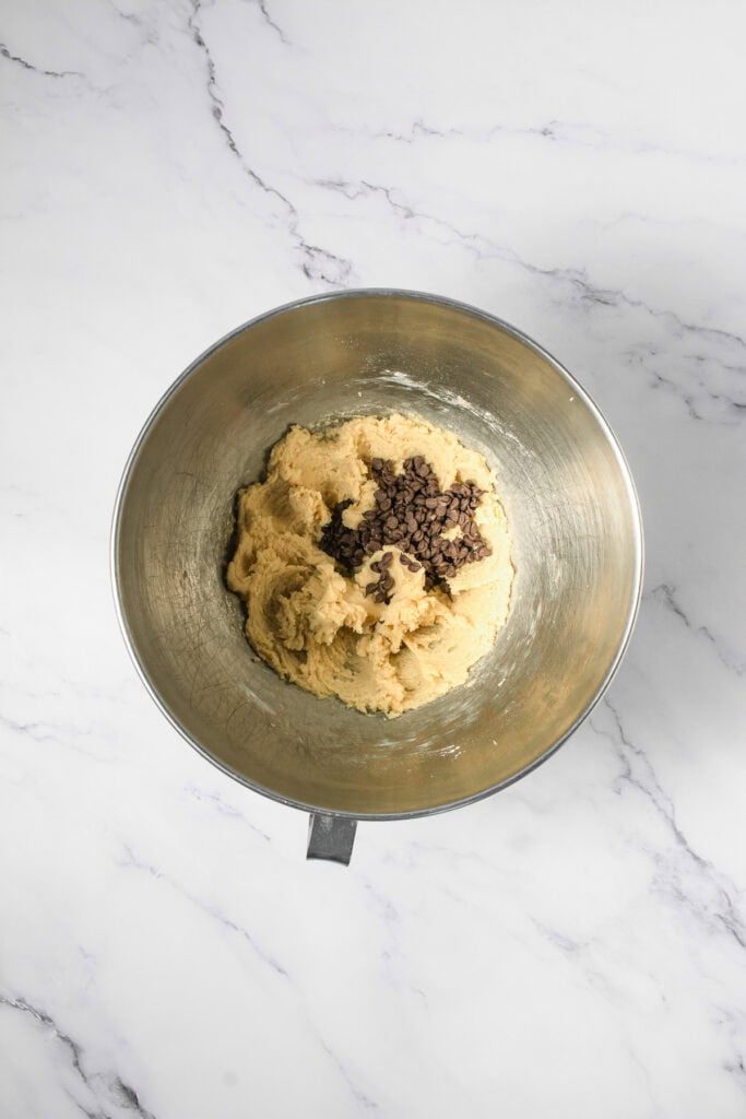Overhead view of Crumbl copycat cookie dough with chocolate chips in a metal mixing bowl on a marble surface.
