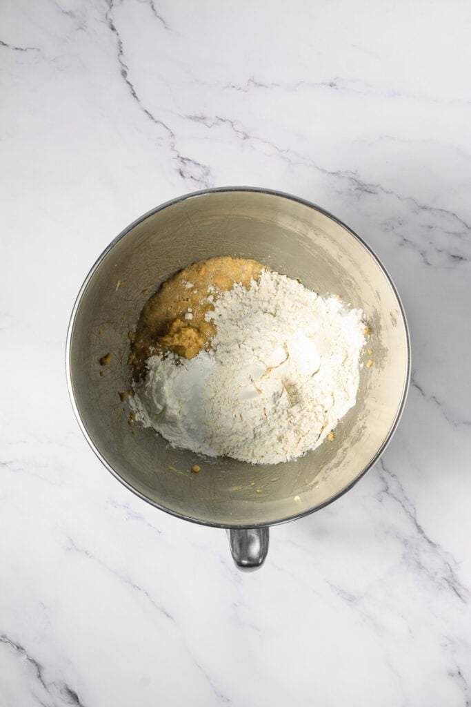 A metal mixing bowl with flour and dough on a white marble surface, ready to be mixed&mdash;perfect for preparing Copycat Cookie Dough Cookies just like the ones from Crumbl.