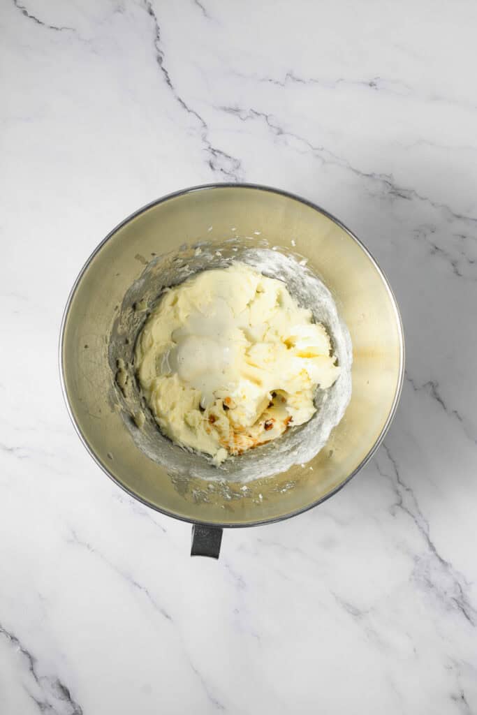 A metal mixing bowl with creamy batter and vanilla, perfect for prepping Cookie Dough Cookies, sits on a white marble surface.