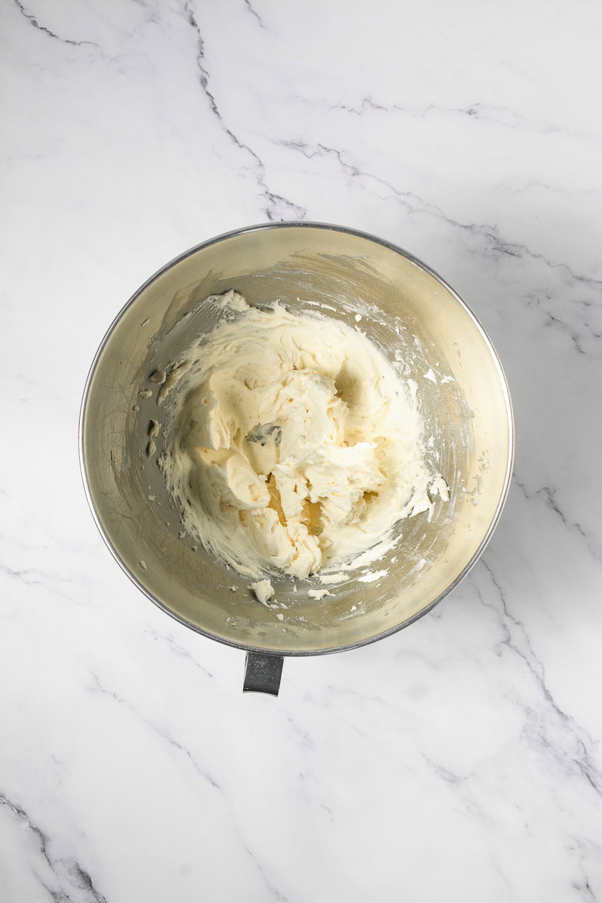 A metal mixing bowl with creamy cookie dough sits on a white marble countertop, perfect for your next Crumbl copycat or favorite cookie recipe.