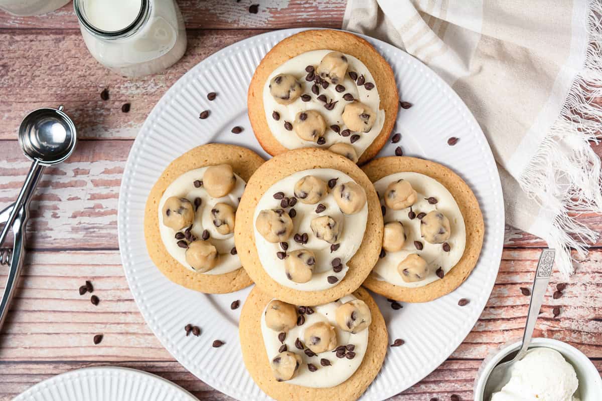 A plate of cookie dough cookies topped with chocolate chips sits next to a glass of milk and a napkin, perfect for anyone seeking the ultimate Crumbl copycat cookie recipe.