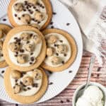 Large Crumbl copycat cookies with frosting, topped with cookie dough bites and chocolate chips, served next to a bowl of vanilla ice cream.