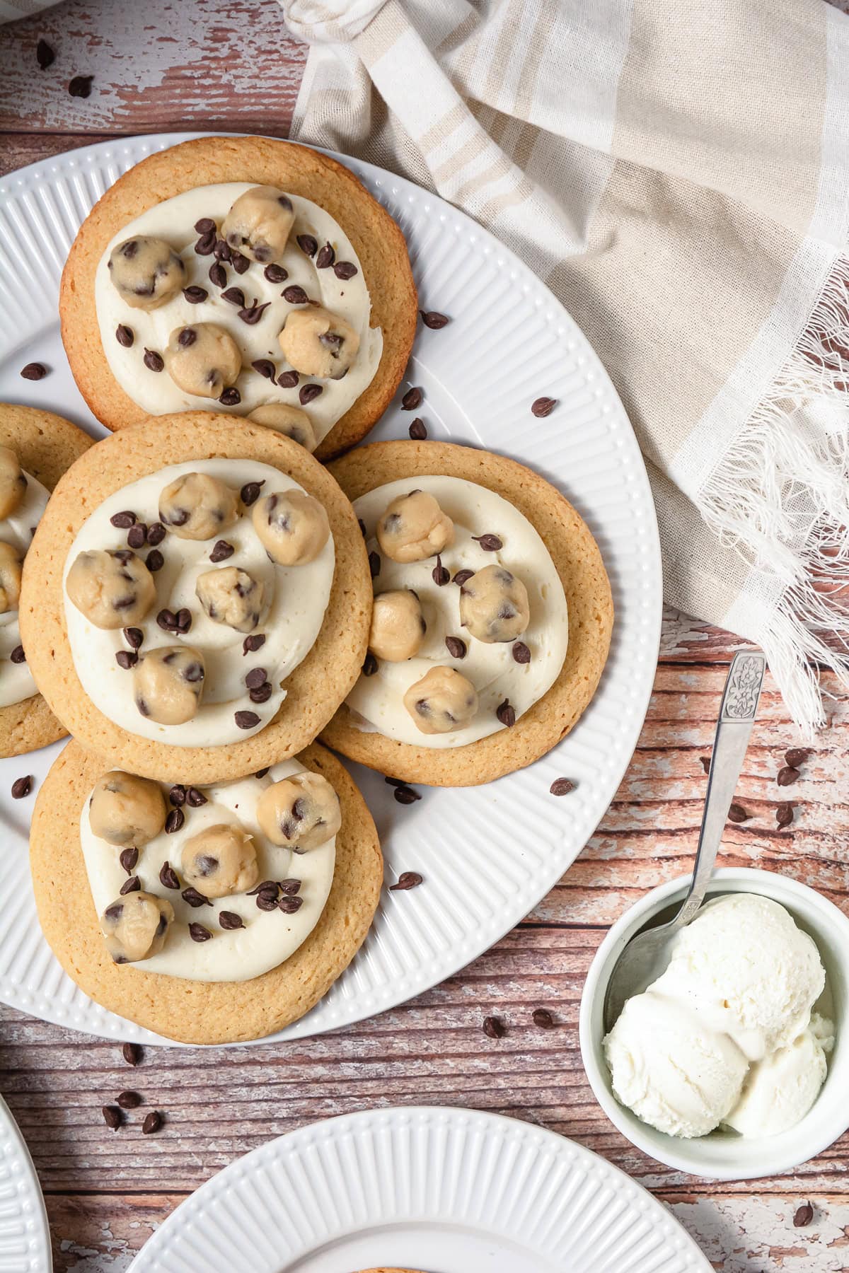 Large Crumbl copycat cookies with frosting, topped with cookie dough bites and chocolate chips, served next to a bowl of vanilla ice cream.