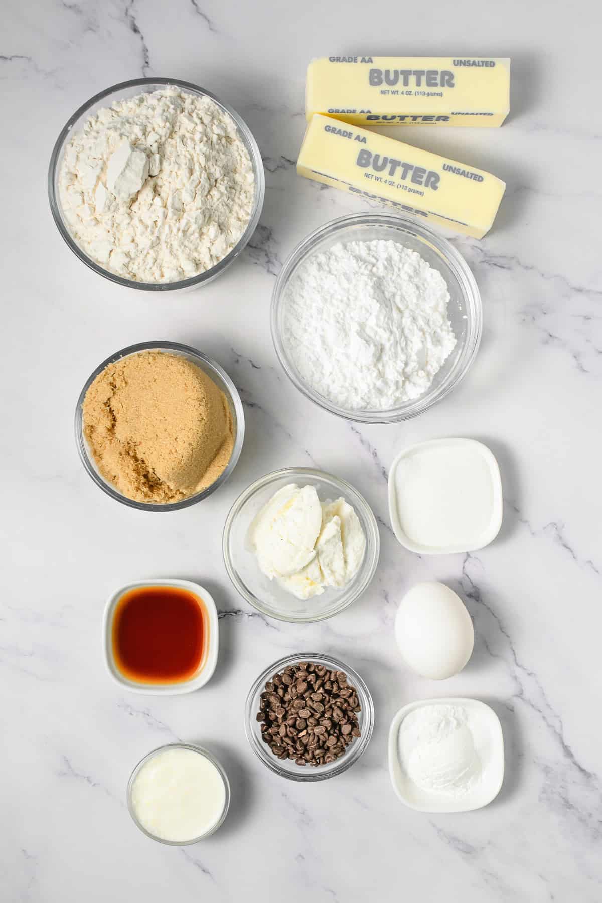 Baking ingredients on a marble surface: flour, sugar, brown sugar, butter, vanilla, egg, chocolate chips, and cream&mdash;everything you need to make Crumbl copycat cookie dough cookies.