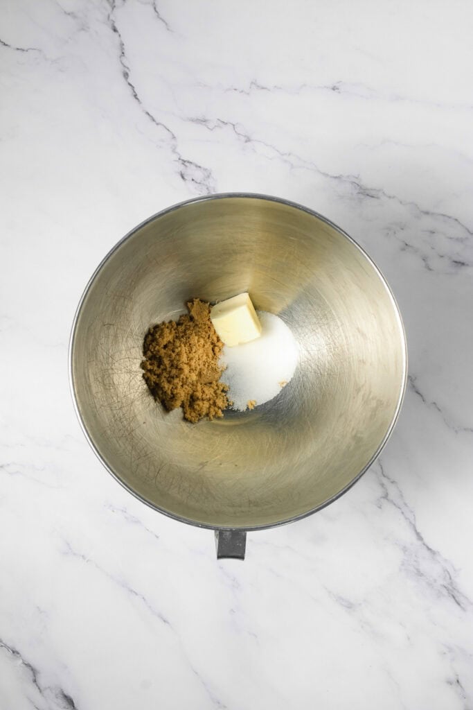 A metal mixing bowl with butter and brown sugar on a white marble surface, ready to be whipped into delicious cookie dough cookies&mdash;perfect for trying your favorite Crumbl copycat cookie recipe.
