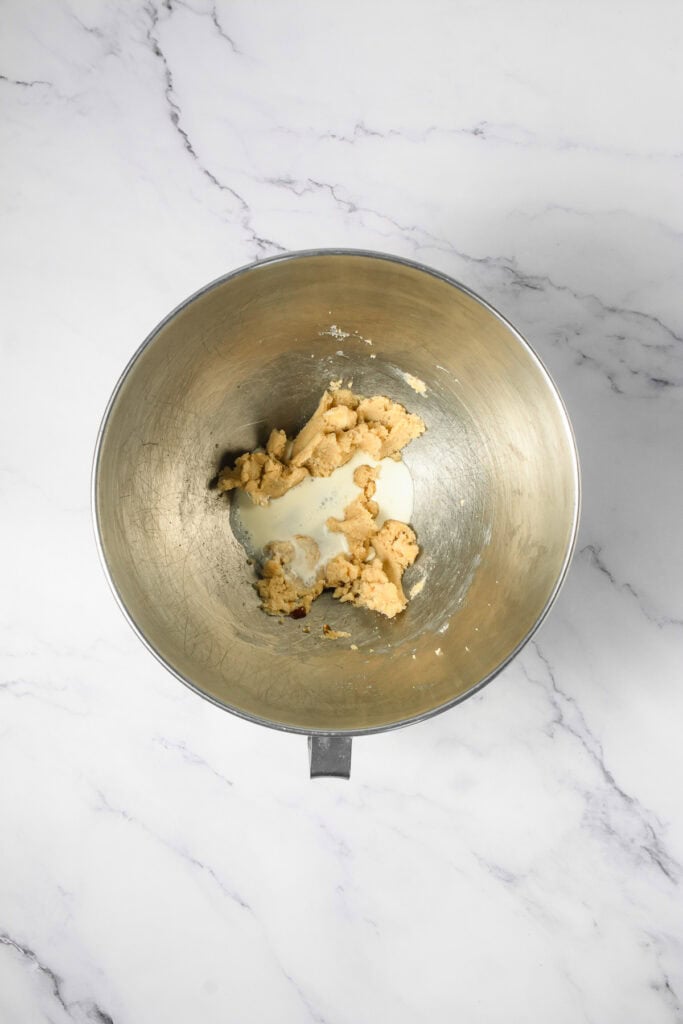 A metal mixing bowl with Crumbl copycat cookie dough and milk on a white marble countertop.