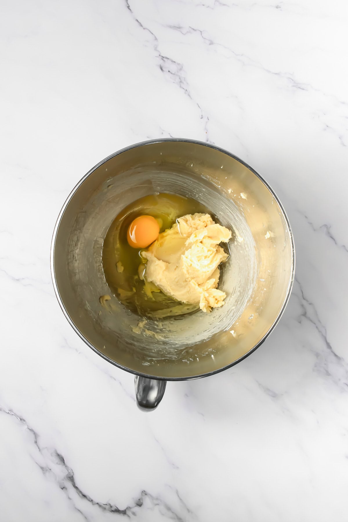 A metal mixing bowl with butter and an egg sits on a white marble surface, ready to create Crumbl copycat frosted Oreo cookies.