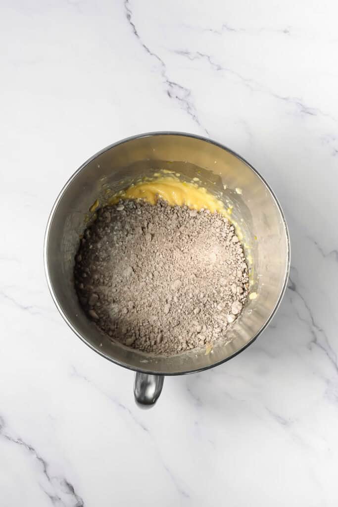 A mixing bowl with yellow batter and cocoa powder on a white marble surface, perfect for whipping up Crumbl Copycat Frosted Oreo Cookies.