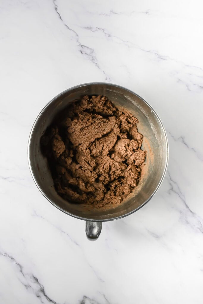 Metal mixing bowl with chocolate cookie dough and crushed Oreo cookies on a marble countertop, viewed from above.