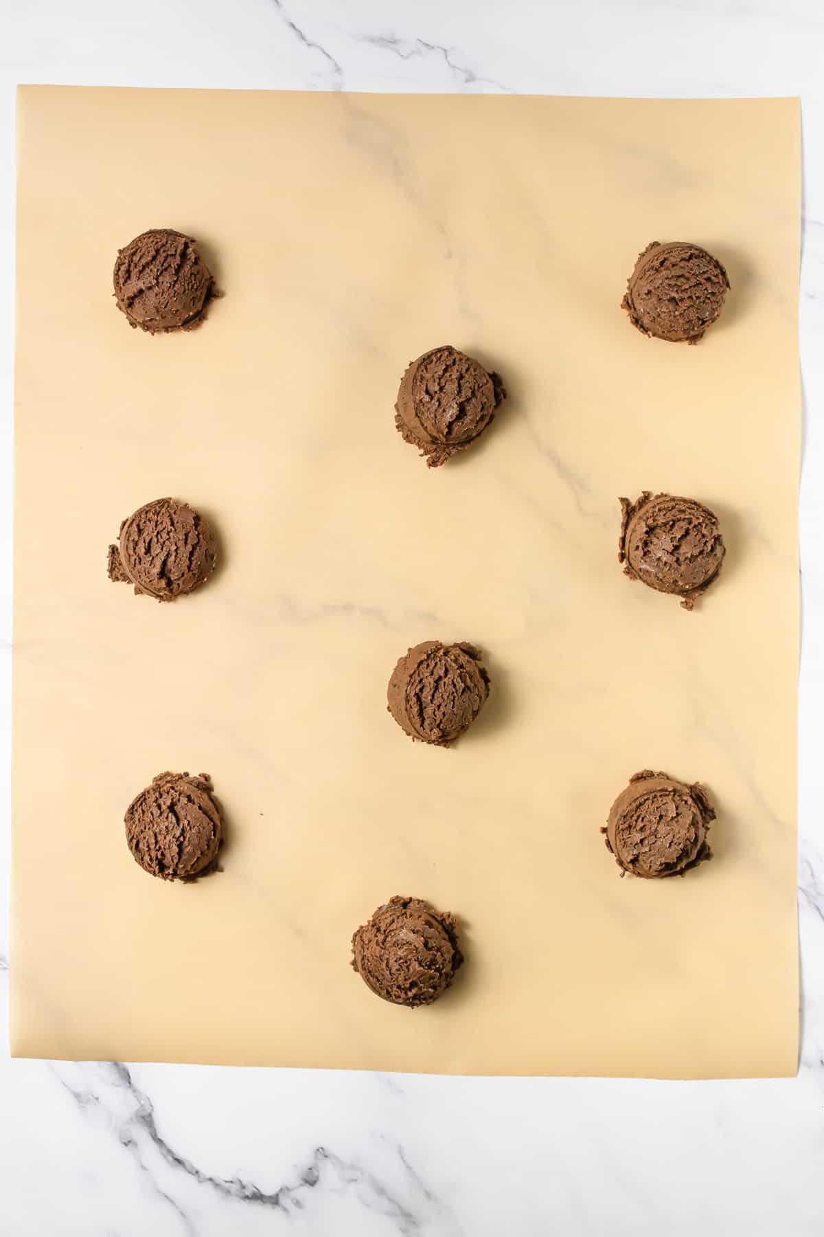 Nine scoops of Crumbl Copycat chocolate cookie dough on parchment paper, arranged in a grid on a marble surface.