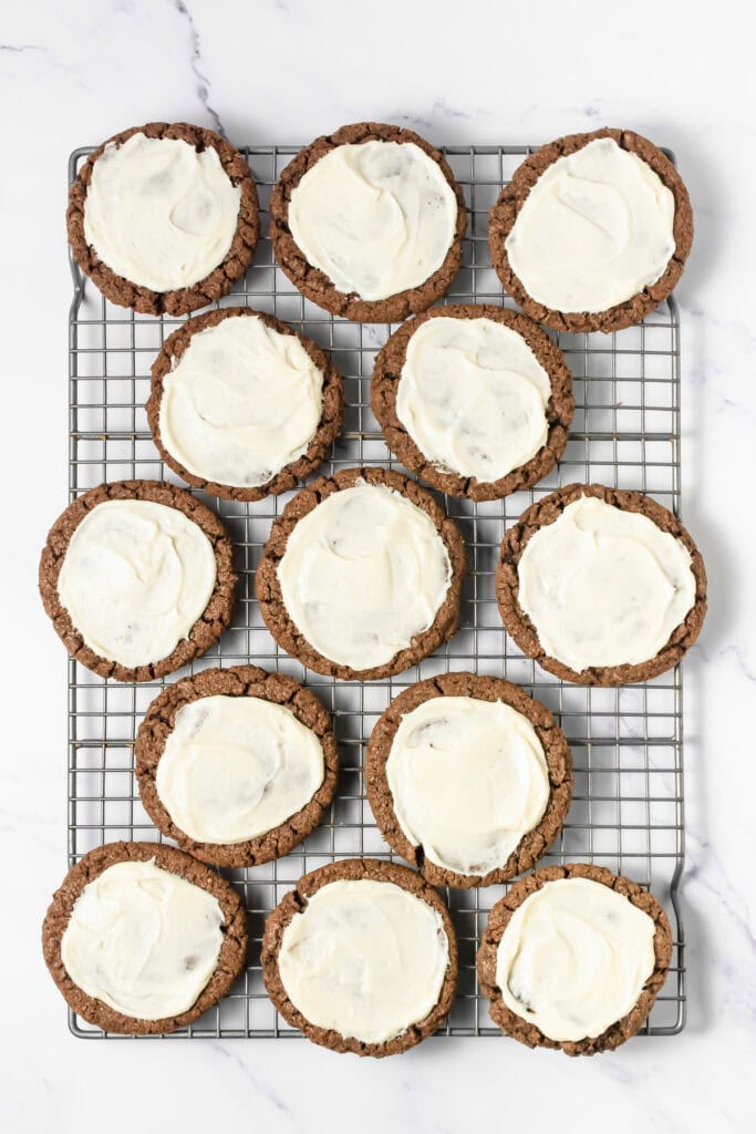Frosted Oreo cookies with white frosting are arranged on a cooling rack over a white marble surface, perfect for anyone seeking a Crumbl copycat treat.