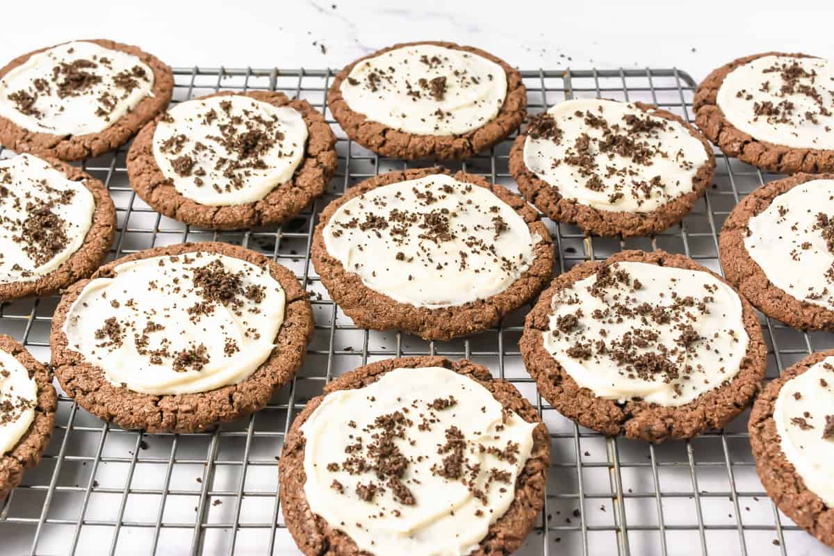 Inspired by Crumbl Copycat recipes, these frosted Oreo cookies feature rich chocolate cookies topped with creamy white frosting and a sprinkle of chocolate crumbs, all cooling on a rack.