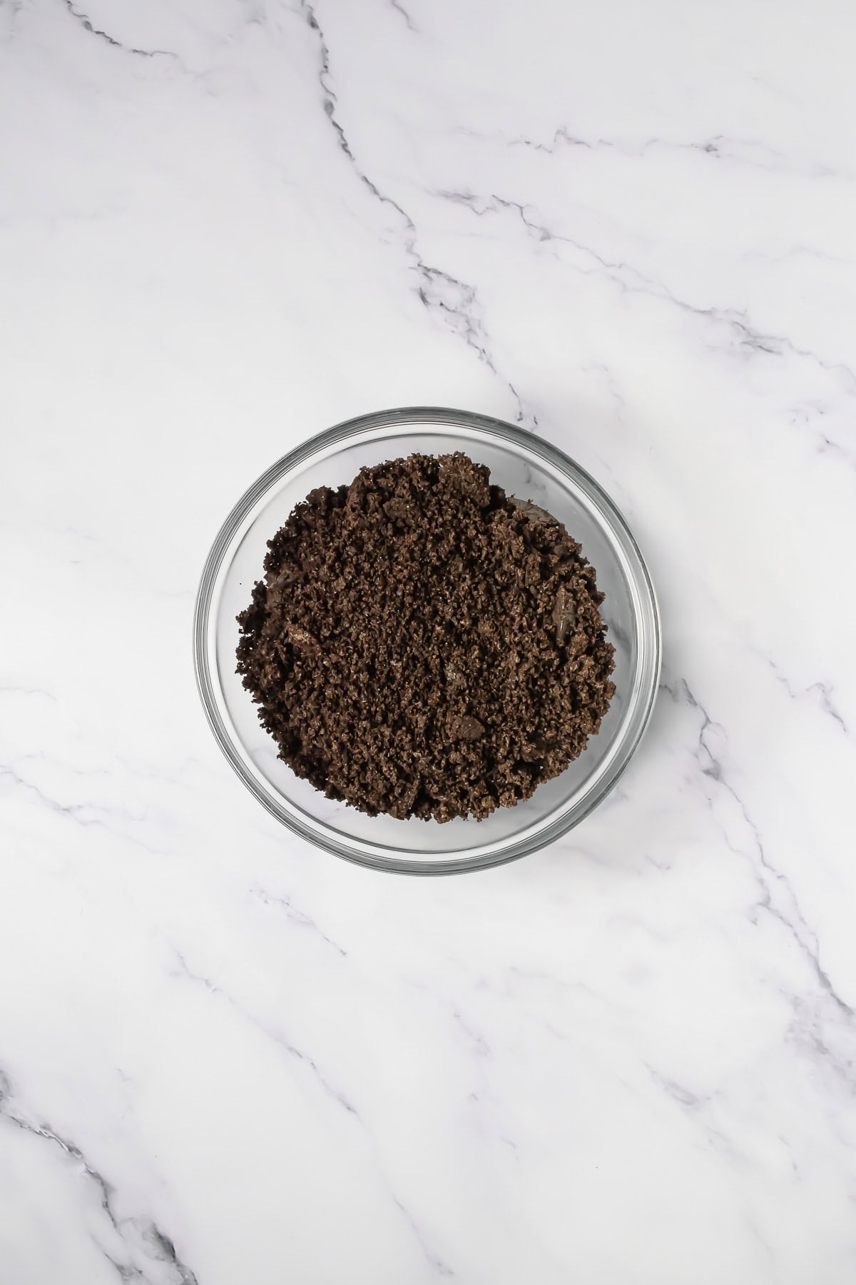 A glass bowl filled with crumbled Oreo cookies sits on a white marble surface, perfect for making Crumbl copycat desserts.